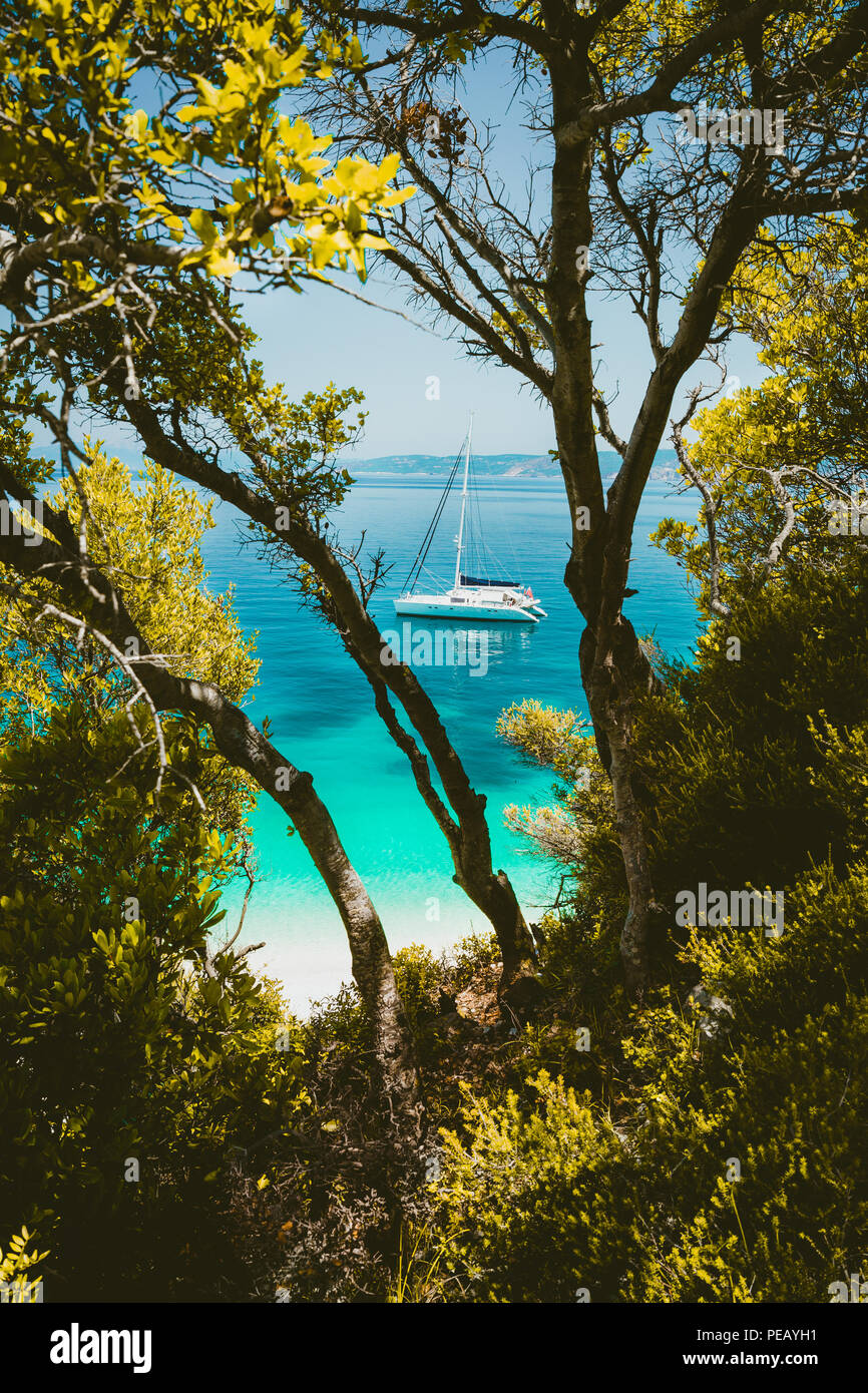Weißen Katamaran Yacht in einem klaren blauen transparenten Meer Wasser Oberfläche verborgen von Zweigniederlassungen von Pine Tree eingerahmt. Erstaunlich Paradies träumen wie Fteri Beach Lagoon, Kefalonia, Griechenland Stockfoto