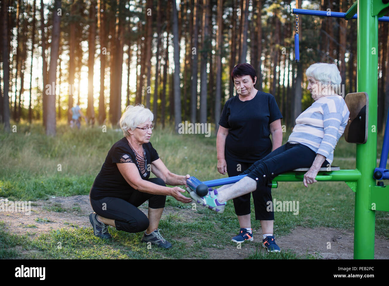 Ältere Frau auf einer Sport Simulator im Park, zwei erwachsene Frauen helfen, ihre Übungen zu tun. Stockfoto