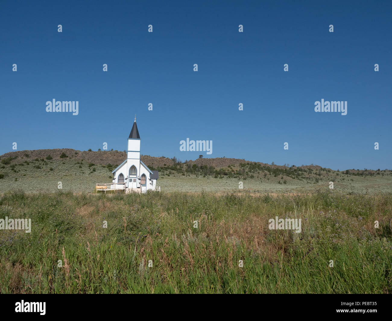 Die alte Weiße Schindeln Trinity Lutheran Church in Lennep Montana mit Hügeln, Salbei Pinsel und blauen Himmel im Hintergrund. Stockfoto