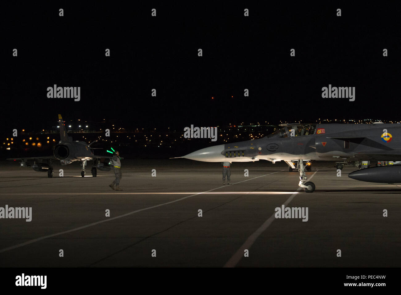 Die kolumbianische Luftwaffe Kfir Kampfjet Crew Chief Signale a Kfir Piloten auf der Flightline in Vorbereitung zu einer Nacht mission Flug, während ein anderes Kfir Taxis während der Red Flag 18-3 an der Nellis Air Force Base, Nev, 31. Juli 2018. Die kolumbianische Luftwaffe Kfir figher Jets training neben der US-Streitkräfte für Red Flag 18-3 in realistischen Air-to-Air Combat Training Szenarien. (U.S. Air Force Foto: Staff Sgt. Angela Ruiz) Stockfoto