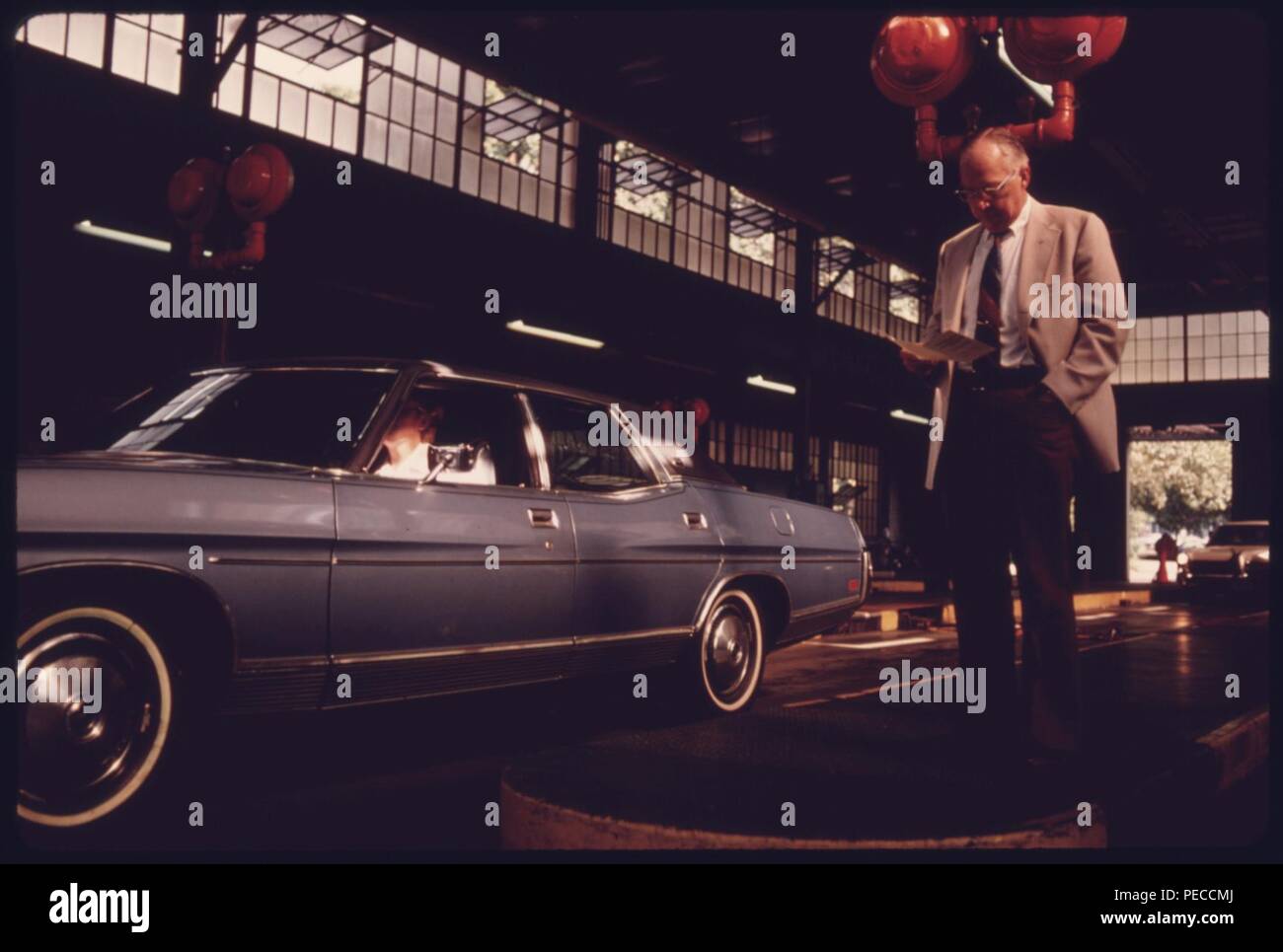 Als sein Auto wird getestet, ein Kraftfahrer liest über eine kostenlose Broschüre über Abgasemissionen an einem Auto Abgasuntersuchung Station in der Innenstadt von Cincinnati, Ohio... 08-1975 Stockfoto
