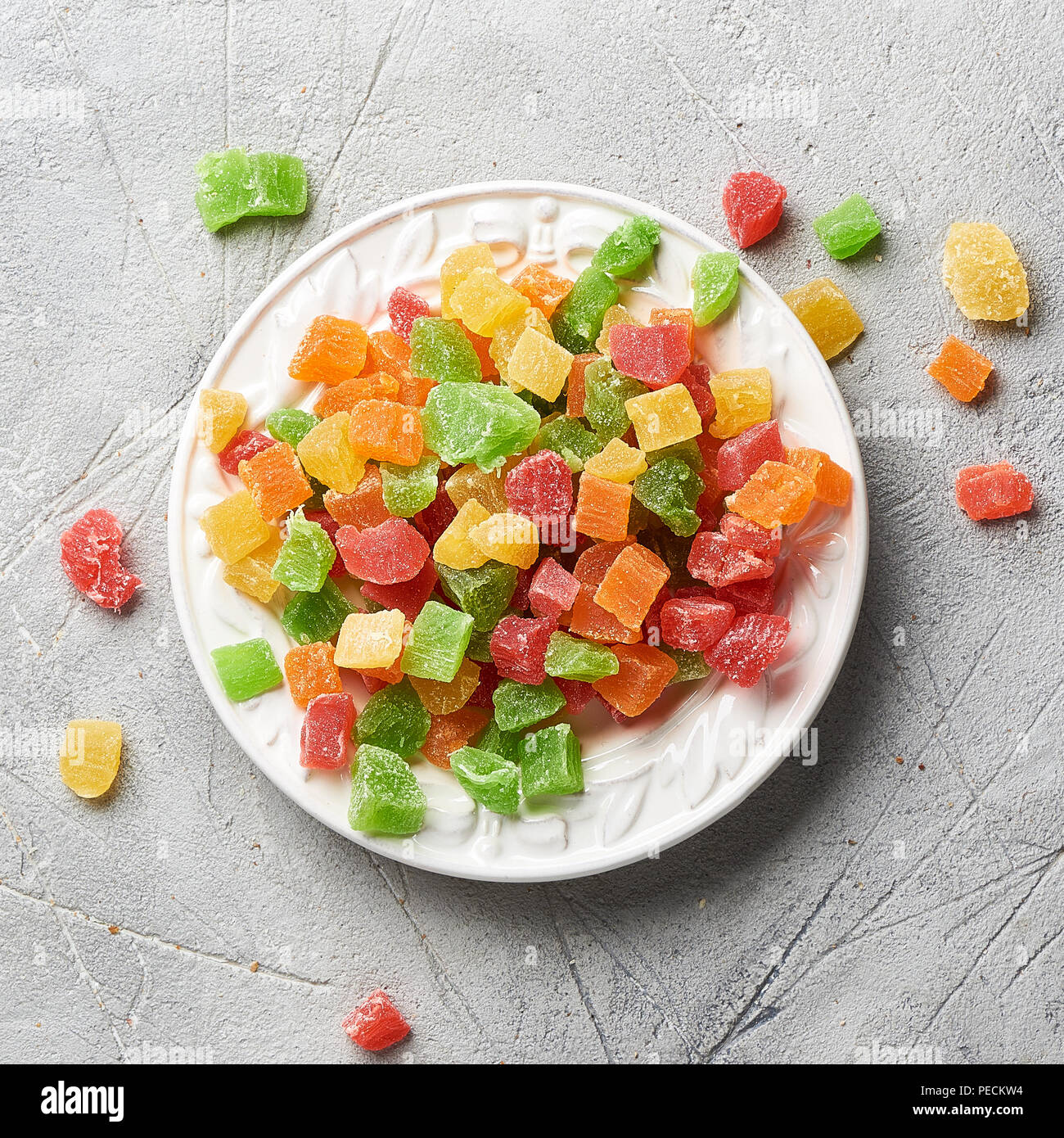 Würfel von getrockneten Aprikosen, Kiwi, Mango, Ananas und Papaya auf weiße Platte. Kandierte Früchte über grauen Hintergrund. Ansicht von oben. Stockfoto