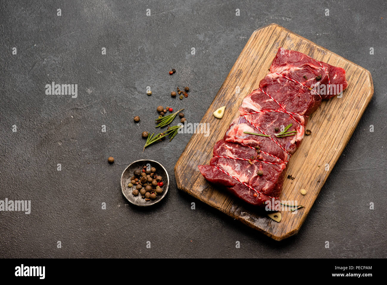 Rohes Fleisch mit Gewürzen und Rosmarin auf Holzbrett. Frisches Rindfleisch. Bereit zum Rösten. Ansicht von oben. Stockfoto