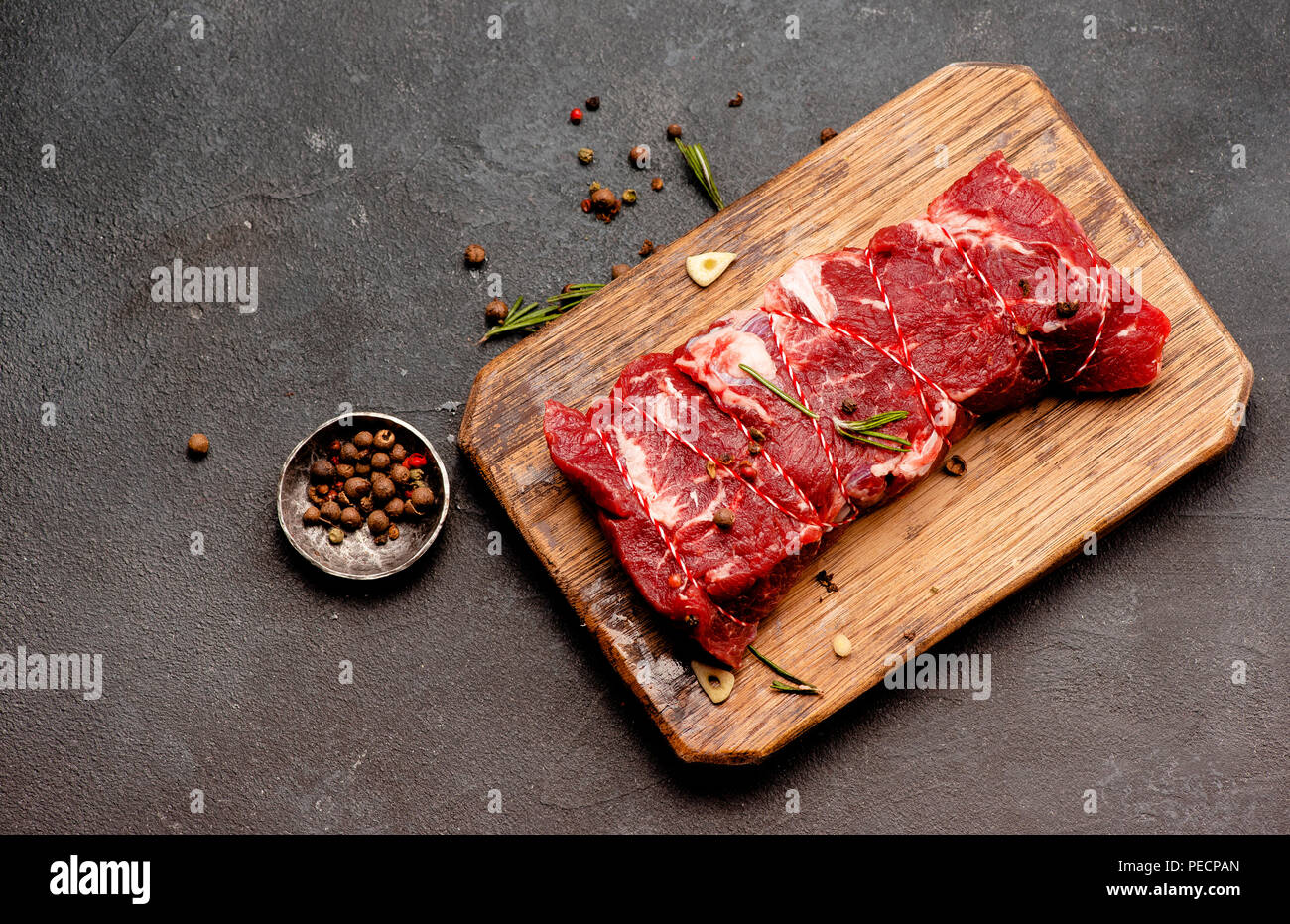 Rohes Fleisch mit Gewürzen und Rosmarin auf Holzbrett. Frisches Rindfleisch. Bereit zum Rösten. Ansicht von oben. Stockfoto