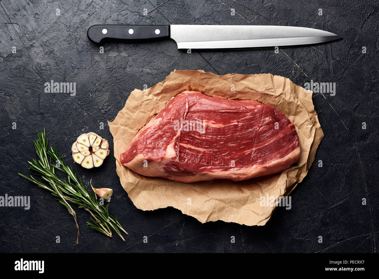 Rohe frische marmoriertes Fleisch Black Angus Steak und Fleisch Messer. Fleisch auf schwarzen Hintergrund mit Rosmarin, Gewürze, Olivenöl und Knoblauch. Ansicht von oben. Stockfoto