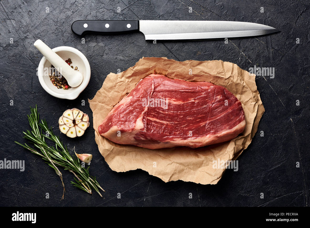 Rohe frische marmoriertes Fleisch Black Angus Steak und Fleisch Messer. Fleisch auf schwarzen Hintergrund mit Rosmarin, Gewürze, Olivenöl und Knoblauch. Ansicht von oben. Stockfoto