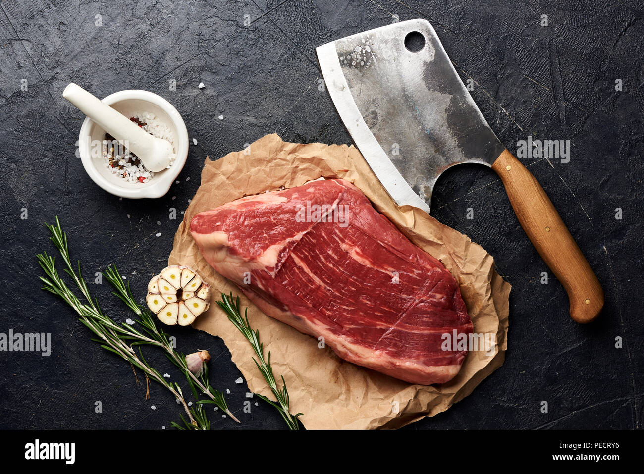Rohe frische marmoriertes Fleisch Black Angus Steak und Fleisch Cleaver. Fleisch auf schwarzen Hintergrund mit Rosmarin, Gewürze, Olivenöl und Knoblauch. Ansicht von oben. Stockfoto