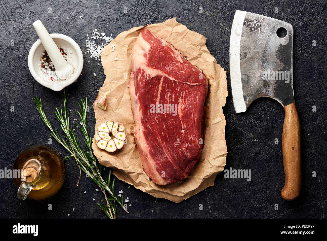 Rohe frische marmoriertes Fleisch Black Angus Steak und Fleisch Cleaver. Fleisch auf schwarzen Hintergrund mit Rosmarin, Gewürze, Olivenöl und Knoblauch. Ansicht von oben. Stockfoto