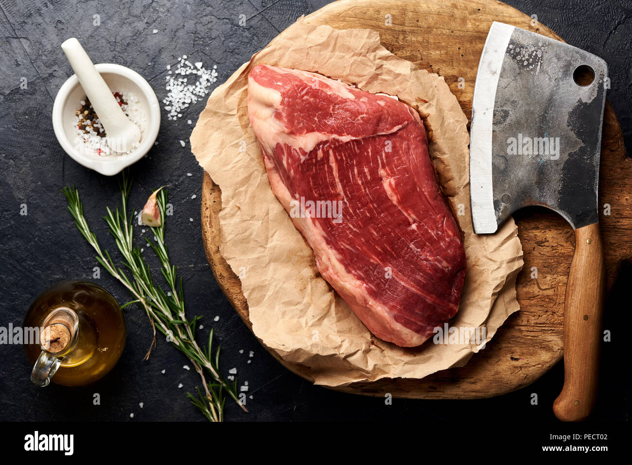 Rohe frische marmoriertes Fleisch Black Angus Steak und Fleisch Cleaver auf Holzbrett. Fleisch auf schwarzen Hintergrund mit Rosmarin, Gewürze, Olivenöl und Knoblauch. Ansicht von oben. Stockfoto