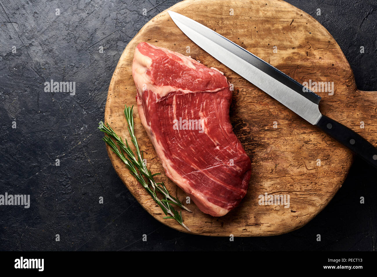Rohe frische marmoriertes Fleisch Black Angus Steak mit Messer für Fleisch auf Holzbrett. Fleisch auf schwarzen Hintergrund mit Rosmarin. Kopieren Sie Platz. Ansicht von oben. Stockfoto