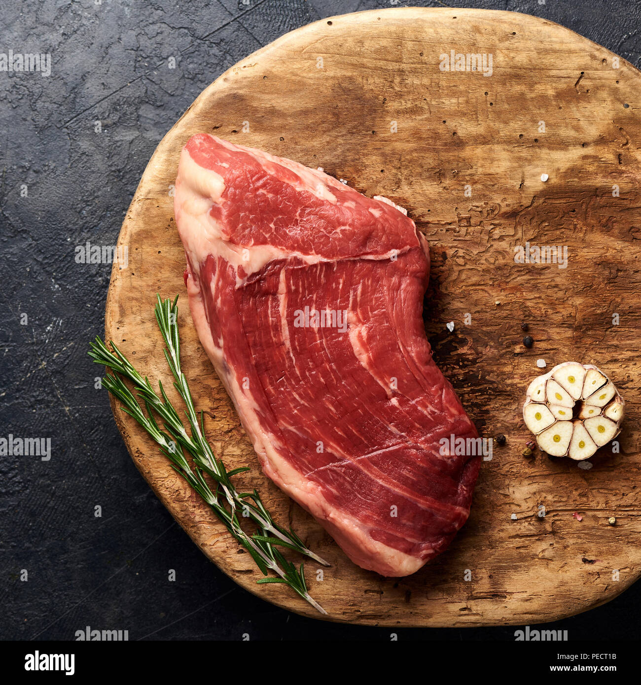 Rohe frische marmoriertes Fleisch Black Angus Steak auf dem Holzbrett. Fleisch auf schwarzen Hintergrund mit Rosmarin und Knoblauch. Kopieren Sie Platz. Ansicht von oben. Stockfoto