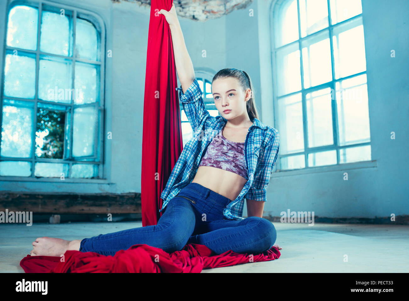 Anmutige gymnast Ausruhen nach Durchführung der Antenne Übung mit roten Stoffen auf Blau alte loft Hintergrund. Jugendliche kaukasischen passen Mädchen. Der Zirkus, Akrobatik, Acrobat, Performer, Sport, Fitness, Gymnastik Konzept Stockfoto