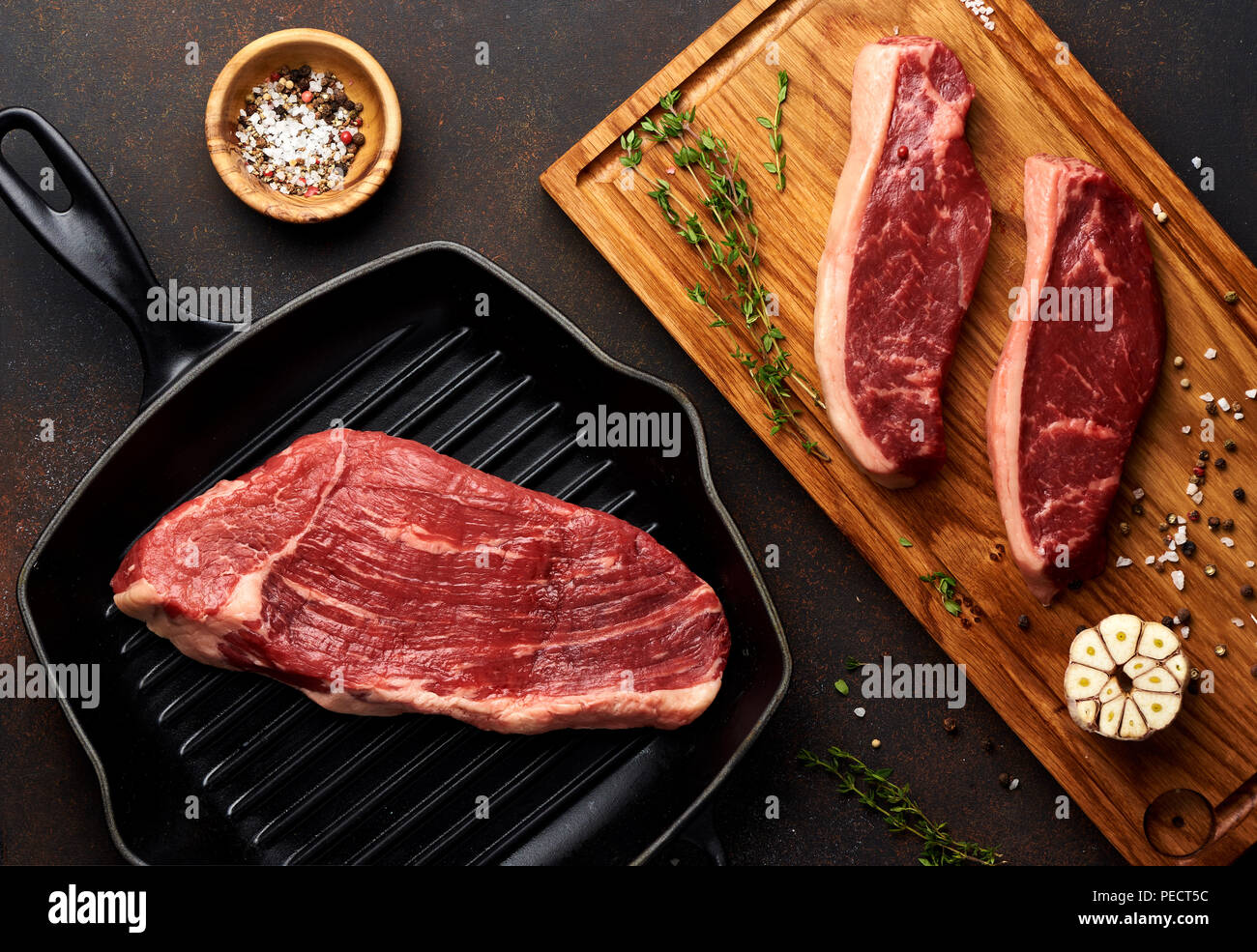 Rohe frische Fleisch Picanha Steak, traditionelle brasilianische Cut mit Thymian, Knoblauch, schwarzer Pfeffer auf Holzbrett. Geschnetzeltes Fleisch Black Angus Steak auf dem Grill eiserne Pfanne. Ansicht von oben. Stockfoto