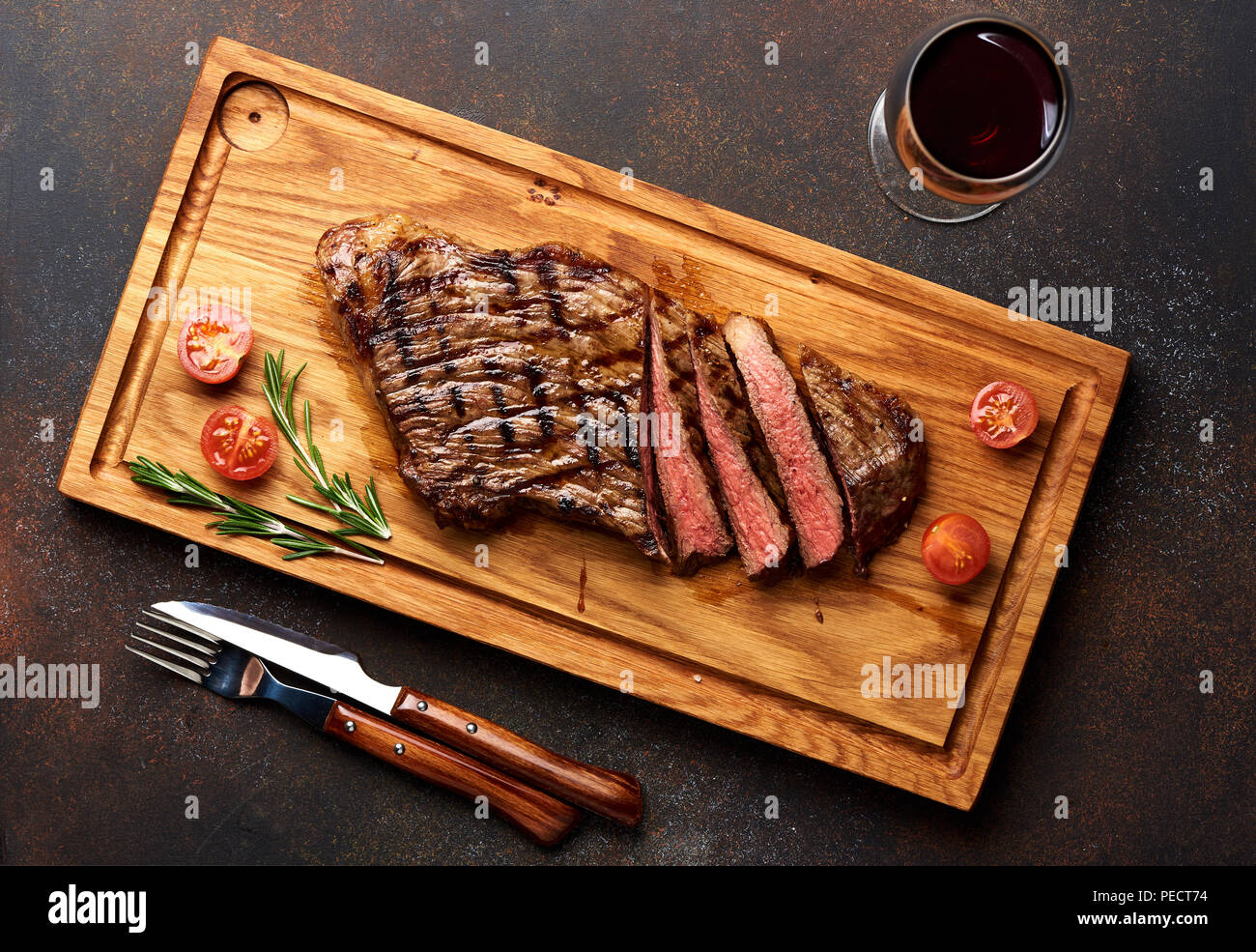 Black Angus Steak vom Grill und einem Glas Rotwein mit Tomaten, Rosmarin auf Fleisch Schneidebrett. Stockfoto