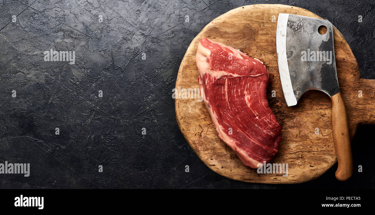 Rohe frische marmoriertes Fleisch Black Angus Steak und Fleisch Cleaver auf Holzbrett. Fleisch auf schwarzem Hintergrund. Kopieren Sie Platz. Ansicht von oben. Stockfoto