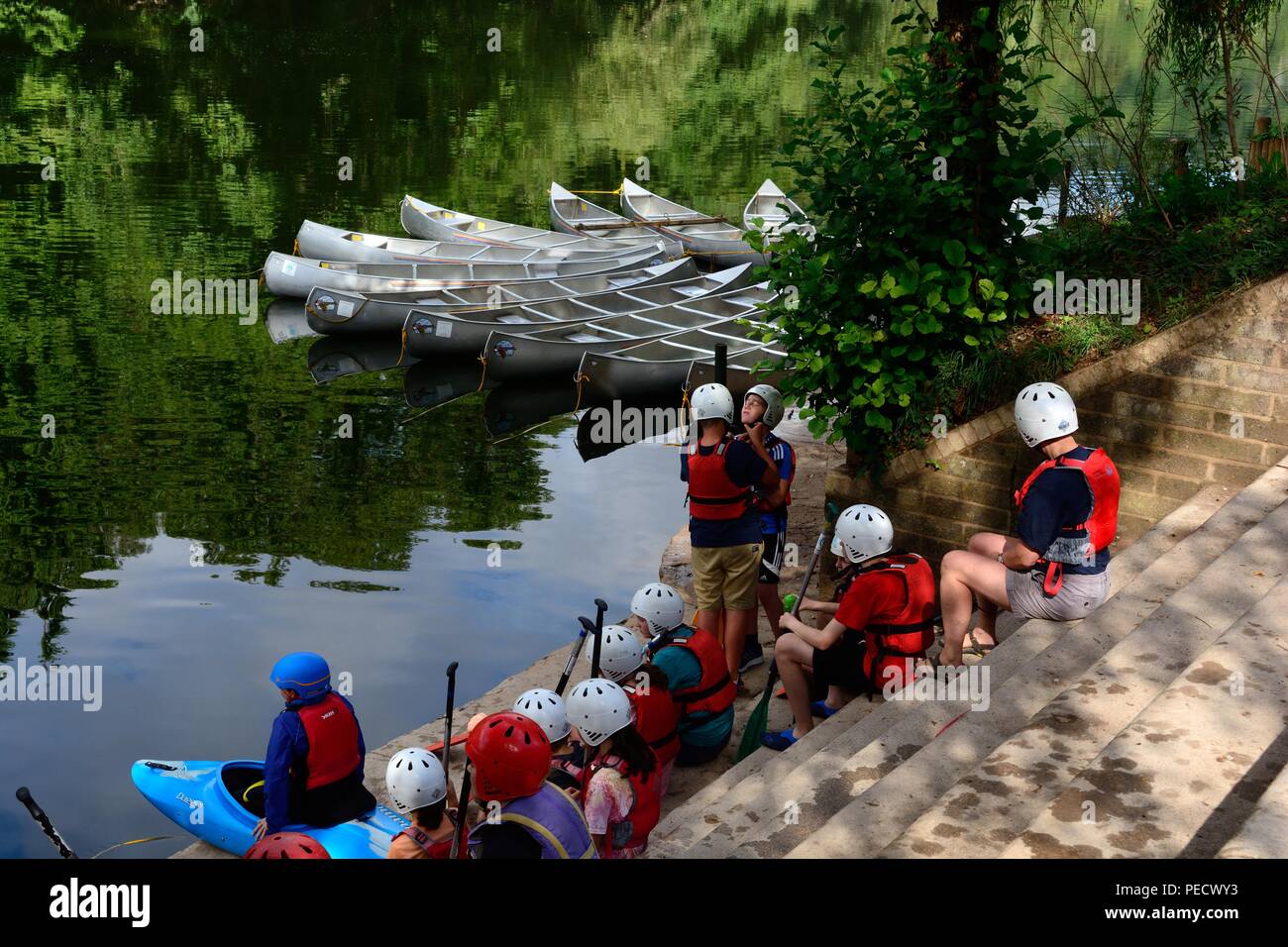 Kinder sitzen auf Schritte, Schwimmwesten und Helme auf der Bank des Wye River warten auf Kanu Unterricht Symonds Yat Stockfoto