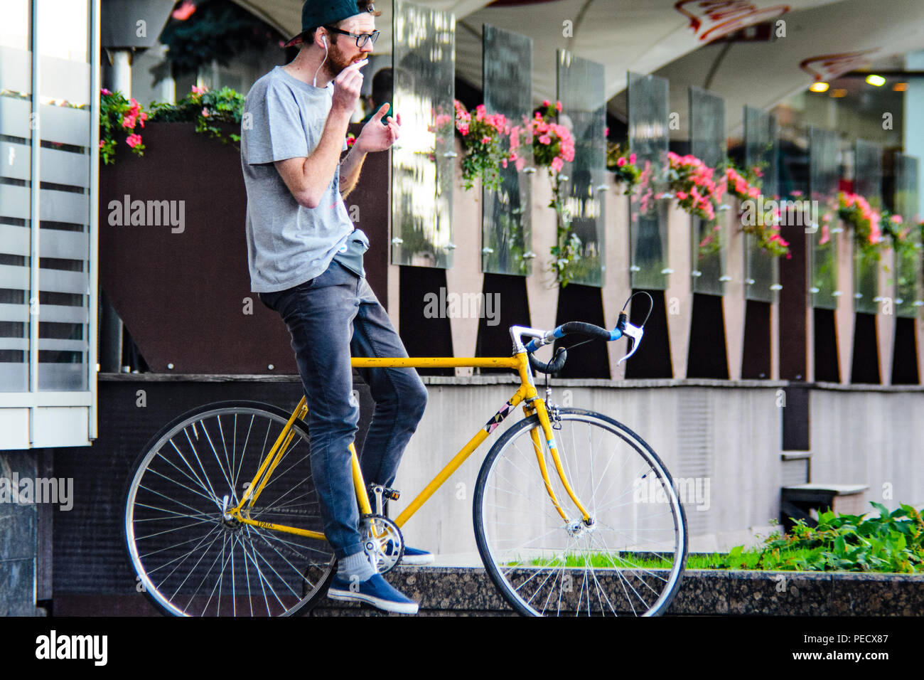 September 22, 2018 Minsk, Weißrussland: Junger Mann stand mit gelben fixie Bike im Stadtbild und macht Hand-roll Zigarette Stockfoto