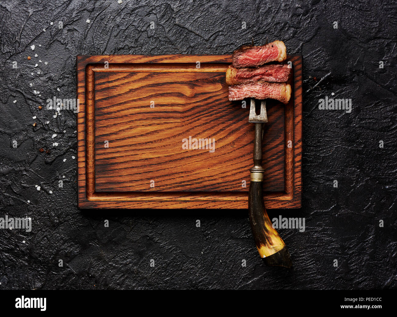 Scheiben von medium gegrilltes Steak auf Fleisch Gabel auf Holz- fleisch Schneidebrett. Schwarz konkreten Hintergrund. Kopieren Sie Platz. Ansicht von oben. Stockfoto