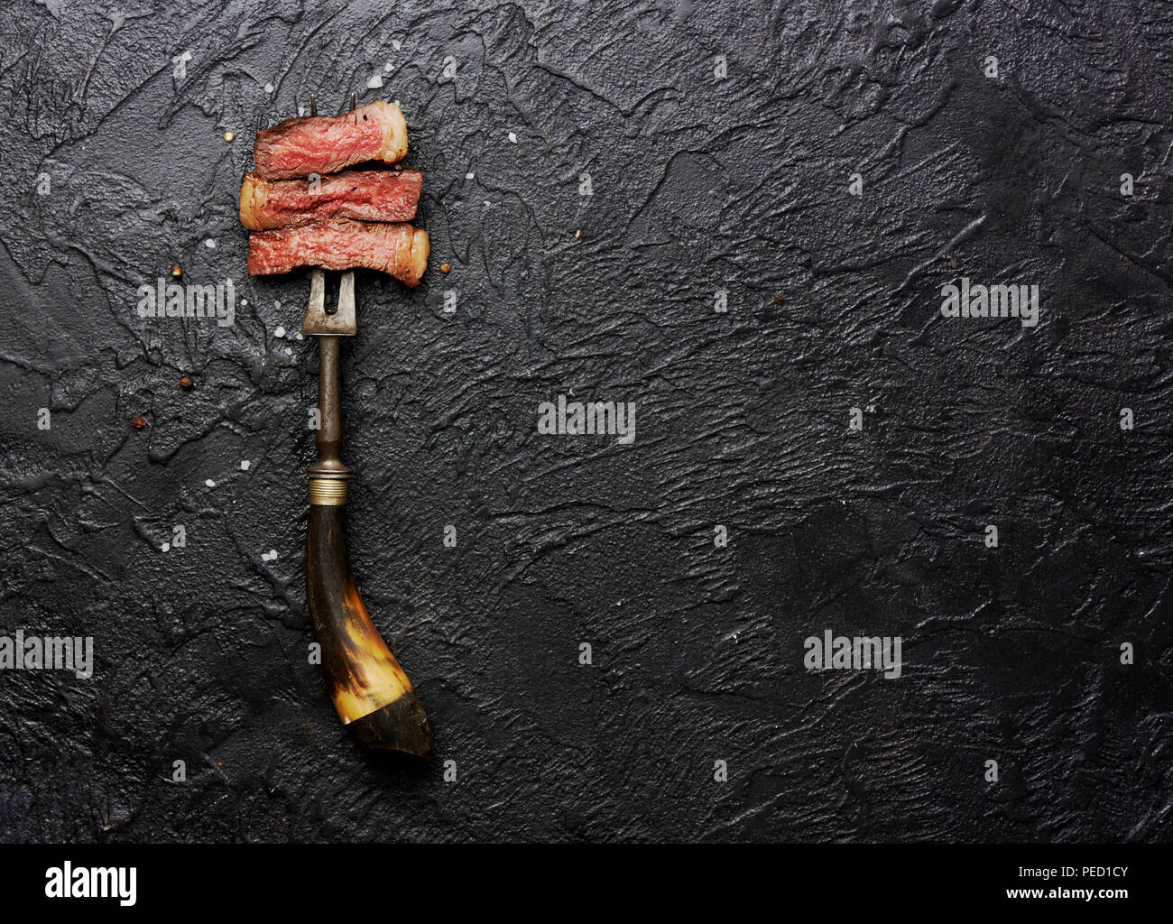 Scheiben von medium gegrilltes Steak auf Fleisch Gabel mit Salz und Pfeffer auf Schwarz konkreten Hintergrund. Kopieren Sie Platz. Ansicht von oben. Stockfoto