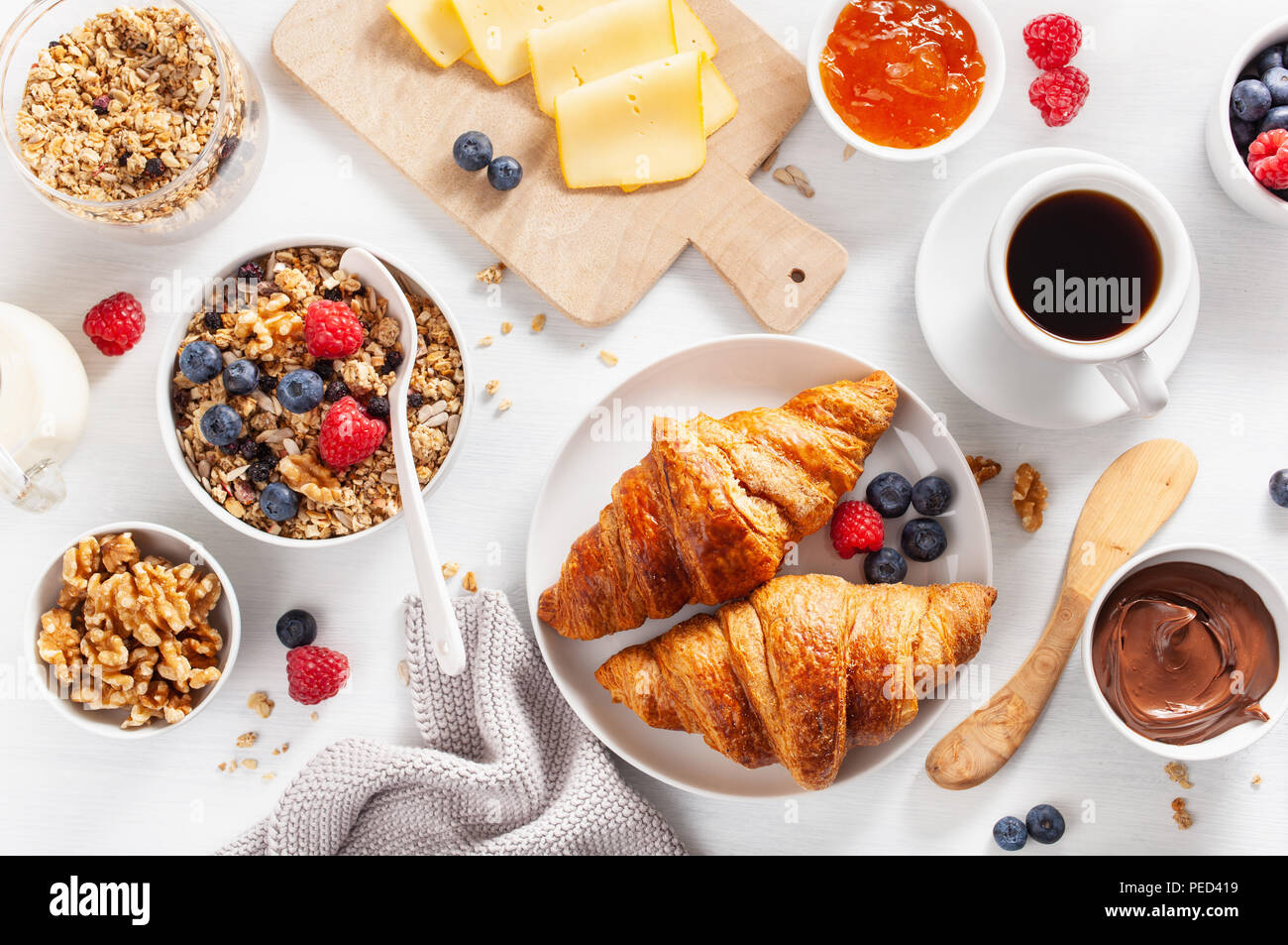 Gesundes Frühstück mit Müsli, Beeren, Nüsse, Croissant, Marmelade, Nutella und Kaffee. Ansicht von oben Stockfoto