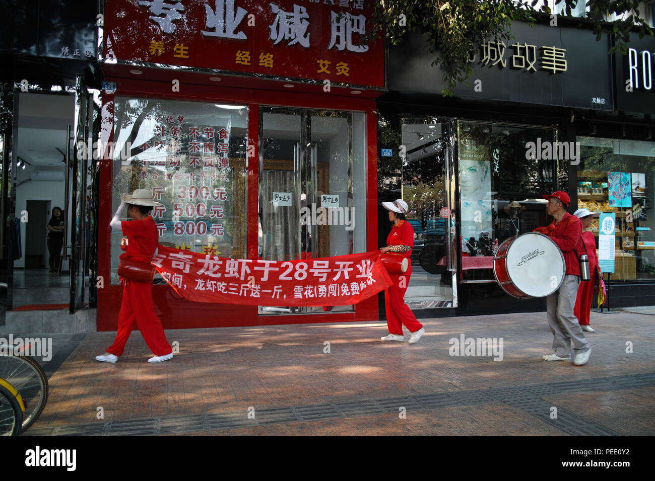 Eine street Marketing Team durch einen Store in der Innenstadt von Chengdu, Sichuan, China. Sie fördern ein Restaurant namens "Legendären Hummer' Stockfoto