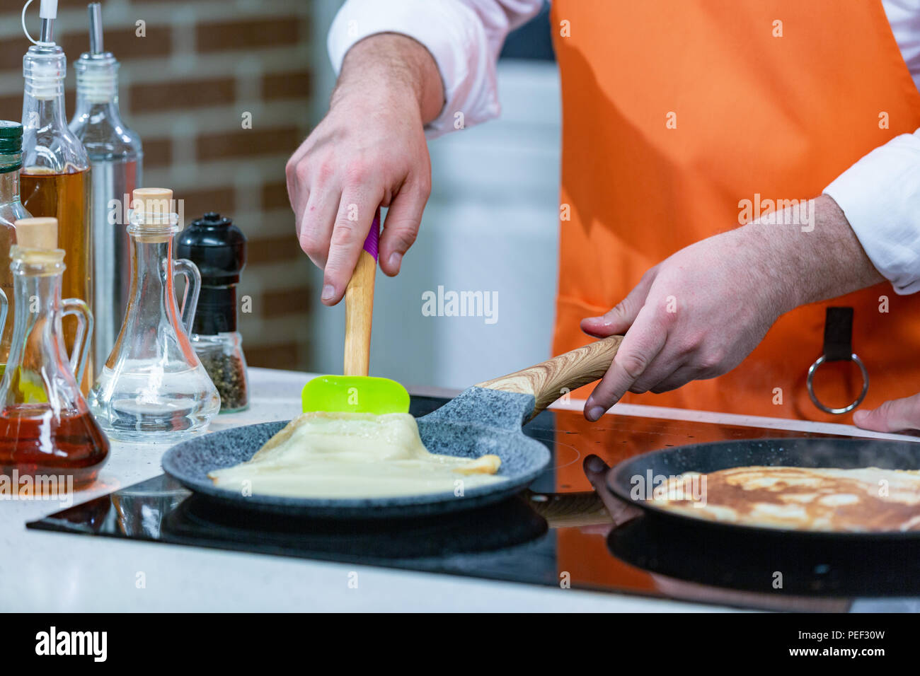 Küche Zubereitung: den Küchenchef in einem hellen Schürze Pommes frische Pfannkuchen in zwei Pfannen Stockfoto