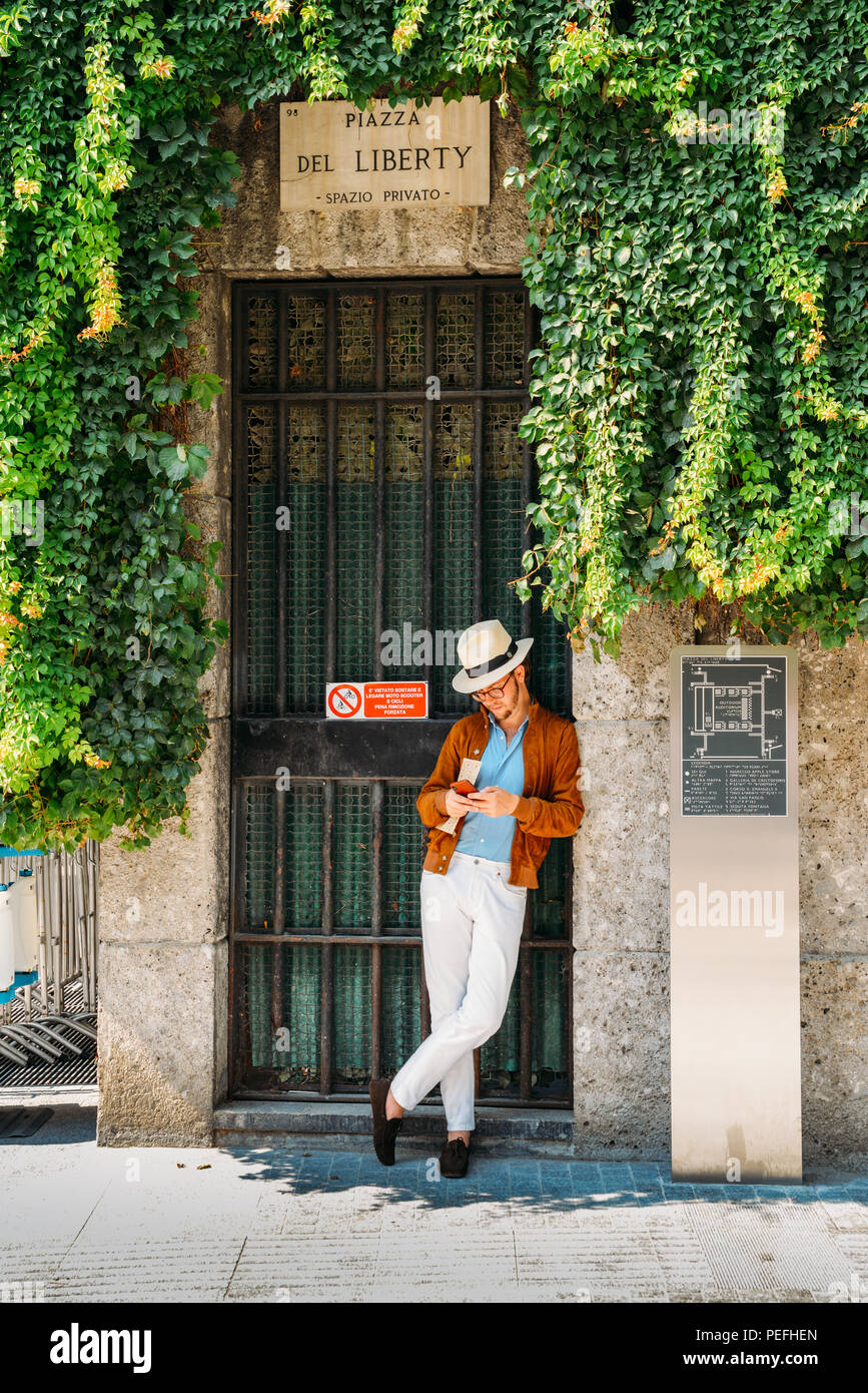 Mailand, Italien - am 26. Juli 2018: Hipster jungen Mann auf das iPhone auf eine Tür Schatten an der Piazza Freiheit in das historische Zentrum von Mailand Stockfoto