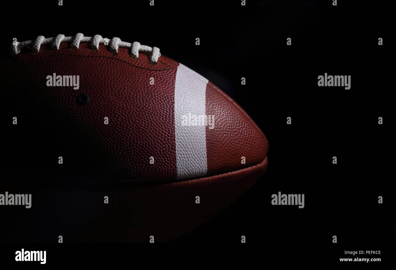 Ein American Football Spiel Ball ist vor einer festen, schwarzen Hintergrund mit Copyspace/text Raum auf der rechten Seite beleuchtet. Stockfoto