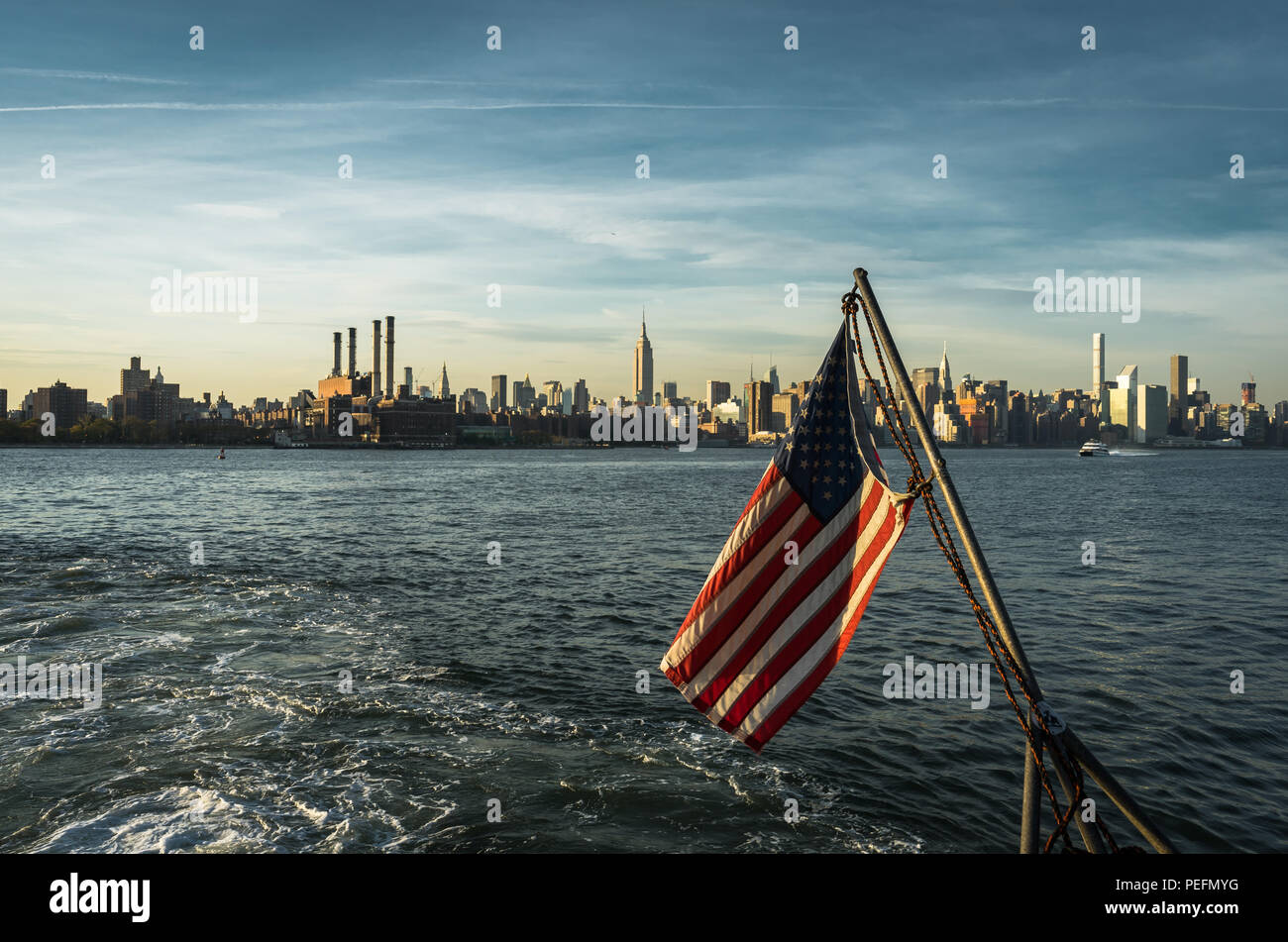 Foto in New York USA übernommen, August 2017: Amerikanische Flagge New York Skyline Citiview Manhattan mit dem Empire State Building Sonnenuntergang von der Fähre Union Ja gesehen Stockfoto