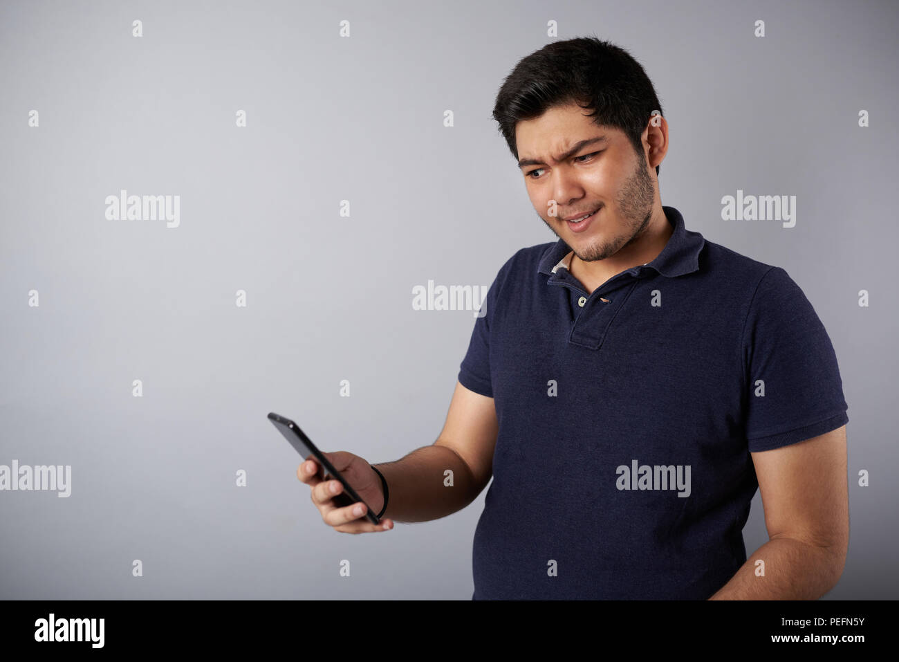 Sorgen junge Mann loking auf dem Smartphone auf grauem Hintergrund Stockfoto