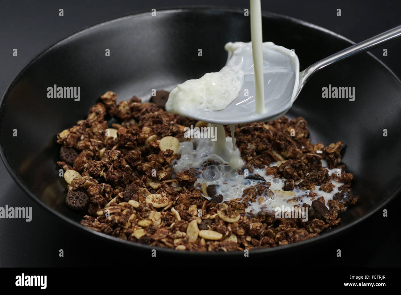 Milch fließt auf Löffel in Schokolade Müsli, Cerealien Stockfoto