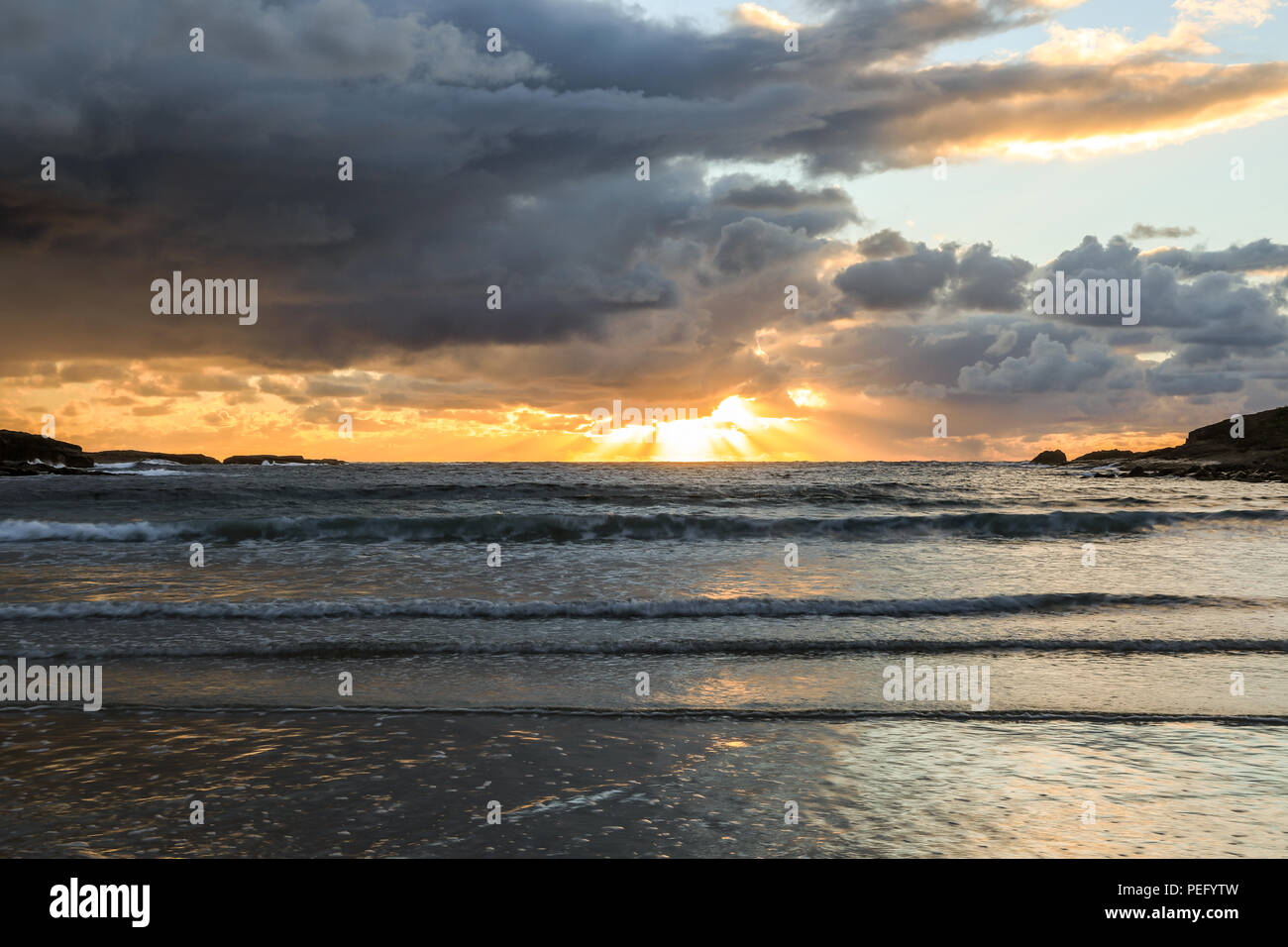 Sonnenaufgang über dem Meer und dem Strand unter bewölktem Himmel Stockfoto