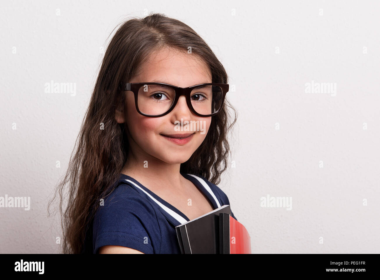 Ein kleines Schulmädchen mit Brille und einheitliche stehend in einem Studio, holding Notepad. Stockfoto