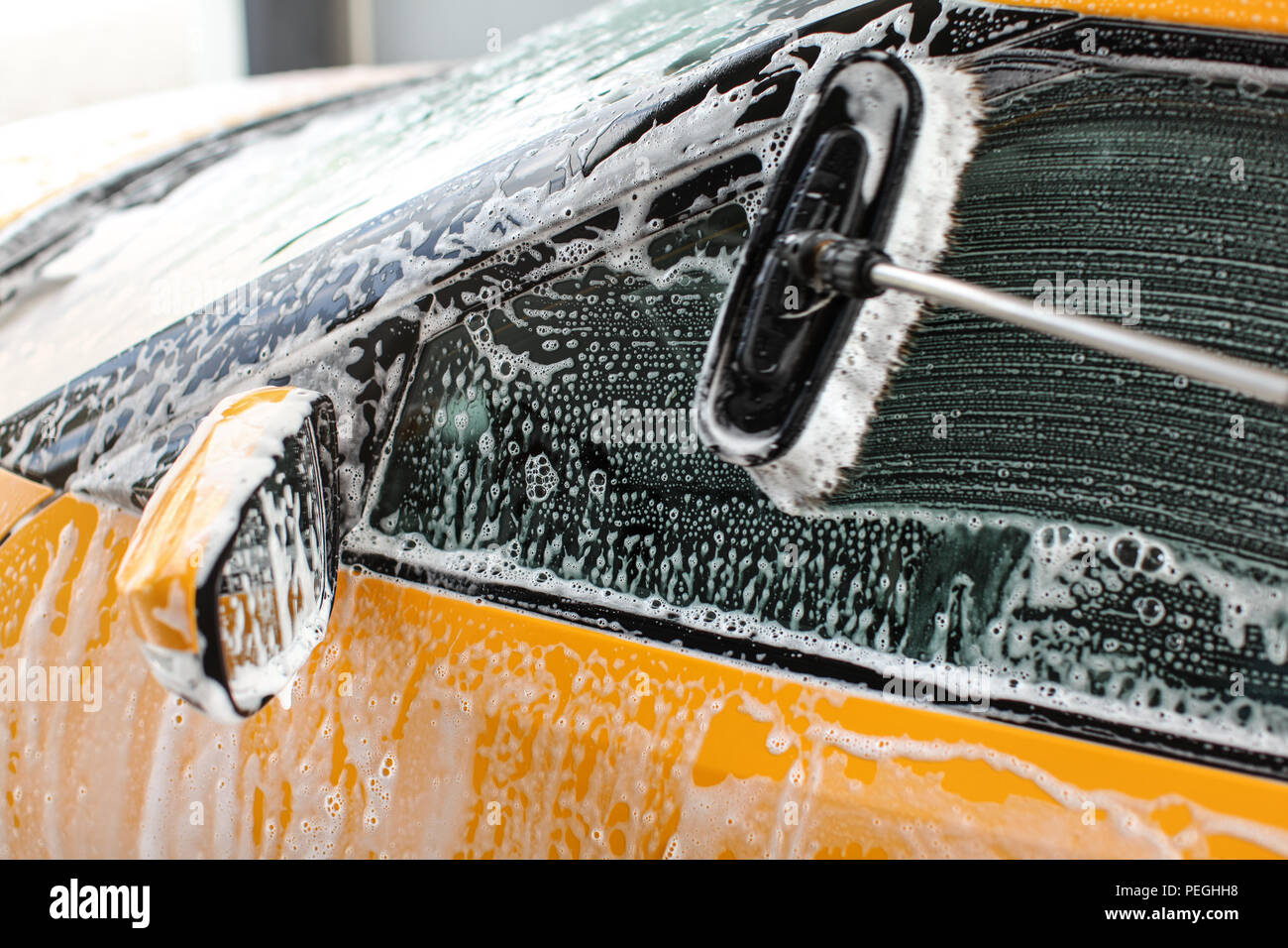 Seitenfenster der gelben Auto in Self-Service-Autowaschanlage gewaschen, Pinsel, Anschläge auf Glas mit Shampoo Schaum bedeckt. Stockfoto