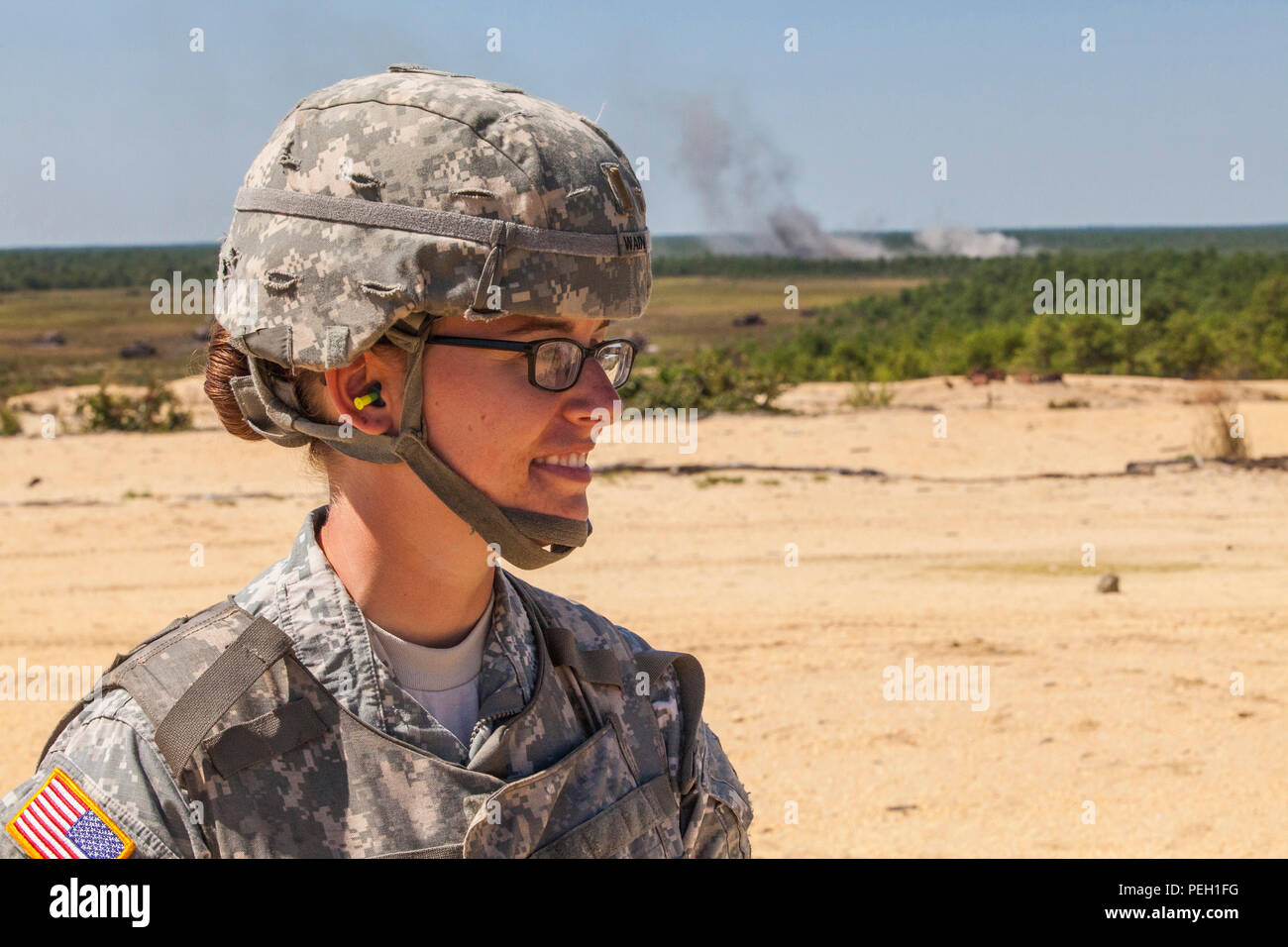 2. Lt. Jennifer Wain, 3-112 th Field Artillery, New Jersey Army National Guard, posiert für ein Portrait als 155 mm Runde aus einer M 777 A2 leichte Haubitze detoniert, die im Hintergrund während einer Live Fire Übung in Joint Base Mc Guire-Dix - Lakehurst, New Jersey, 26.08.2015. Wain, ein Feuer Richtung Offizier mit der 3-112., ist die erste weibliche Combat Arms Officer in der Geschichte der New Jersey Army National Guard. (U.S. Air National Guard Foto von Master Sgt. Mark C. Olsen/Freigegeben) Stockfoto