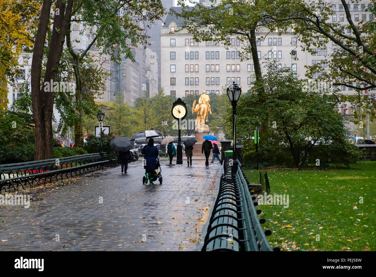 Menschen zu Fuß im Regen in Richtung drehende Uhr Installation von Alicja Kwade im Grand Army Plaza Ende des Central Park, New York Stockfoto