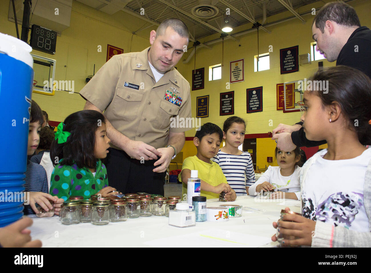 U.S. Navy Petty Officer 1st Class Chris Griggers freiwilligen seiner Zeit zu helfen, Schüler erstellen Pine Cone Schneekugeln Dez.7 an der Cpl. Terry L. Smith Gym im Henderson Halle Teil des Joint Base Myer-Henderson Halle. Die Marines von Henderson Hall lud Schülerinnen von barcroft Volksschule in Arlington, Va., Weihnachten in Henderson Halle zu Feiern, Dekorieren Sugar Cookies, Erstellen von Ornamenten und verbringt Zeit mit Santa. (Joint Base Myer-Henderson Halle PAO Foto von Delonte Harrod) Stockfoto