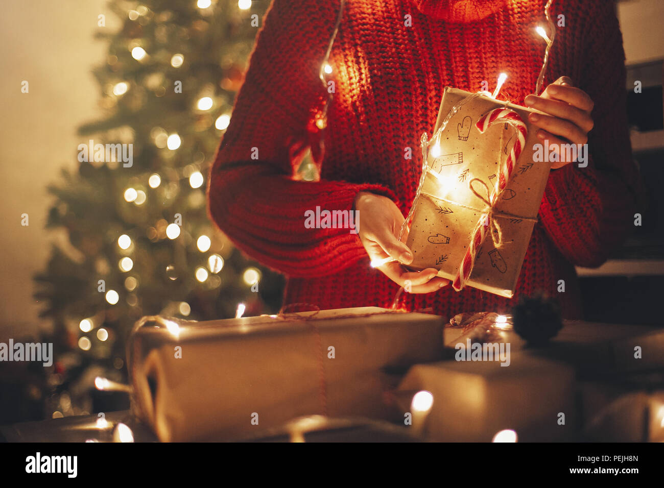 Frohe Weihnachten Konzept. Hände, die Weihnachten in Lichter am Abend festliches Zimmer unter Baum in Beleuchtung vorhanden. Platz für Text. Mädchen Eröffnung Mo Stockfoto