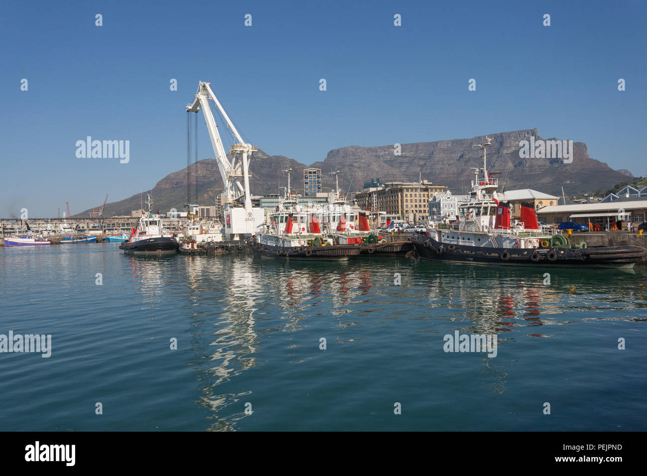 Günstig Schlepper und Kran im Hafen oder Hafen Hafen Kapstadt gegen die Kulisse des Tafelbergs an einem klaren, sonnigen Tag in Afrika Stockfoto