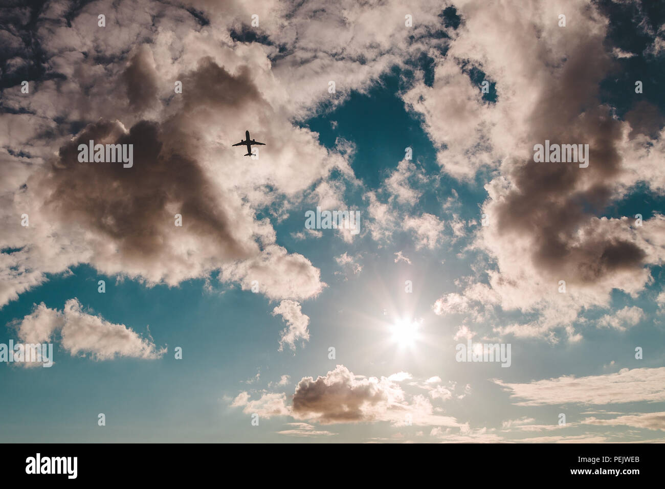 Silhouette eines abfliegenden Flugzeuge gegen einen teilweise bewölktem Himmel mit der Sonne. Stockfoto