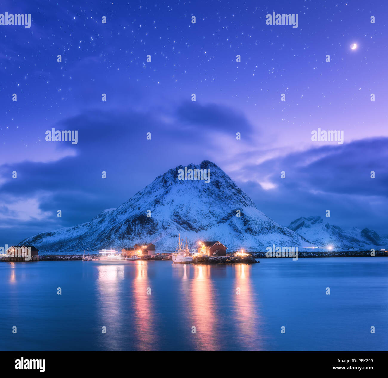 Fischerboote in der Nähe von Pier am Meer gegen Snowy Mountains und starry lila Himmel mit Mond in der Nacht auf den Lofoten Inseln, Norwegen. Winterlandschaft mit Stockfoto