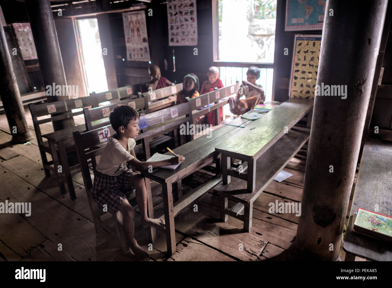 Bagaya Kloster Schule Kinder Inwa Myanmar // INWA, Myanmar — Kinder besuchen Unterricht in einem bestimmten Schulbereich im Bagaya Kloster (auch bekannt als Bagaya Kyaung), einem Teakkloster, das während der Konbaung Dynastie errichtet wurde. Das Kloster ist vollständig aus Teakholz gebaut, unterstützt von 267 riesigen Teakholzpfosten, wobei der größte 60 Meter hoch und 9 Fuß im Umfang ist. Das Kloster Bagaya dient sowohl als religiöse Stätte als auch als Bildungseinrichtung und setzt die traditionelle Rolle der buddhistischen Klöster bei der Bereitstellung von Gemeindeerziehung fort. Das Kloster befindet sich in Inwa (auch bekannt Stockfoto Bagaya Kloster Schule Kinder Inwa Myanmar // INWA, Myanmar — Kinder besuchen Unterricht in einem bestimmten Schulbereich im Bagaya Kloster (auch bekannt als Bagaya Kyaung), einem Teakkloster, das während der Konbaung Dynastie errichtet wurde. Das Kloster ist vollständig aus Teakholz gebaut, unterstützt von 267 riesigen Teakholzpfosten, wobei der größte 60 Meter hoch und 9 Fuß im Umfang ist. Das Kloster Bagaya dient sowohl als religiöse Stätte als auch als Bildungseinrichtung und setzt die traditionelle Rolle der buddhistischen Klöster bei der Bereitstellung von Gemeindeerziehung fort. Das Kloster befindet sich in Inwa (auch bekannt Stockfoto