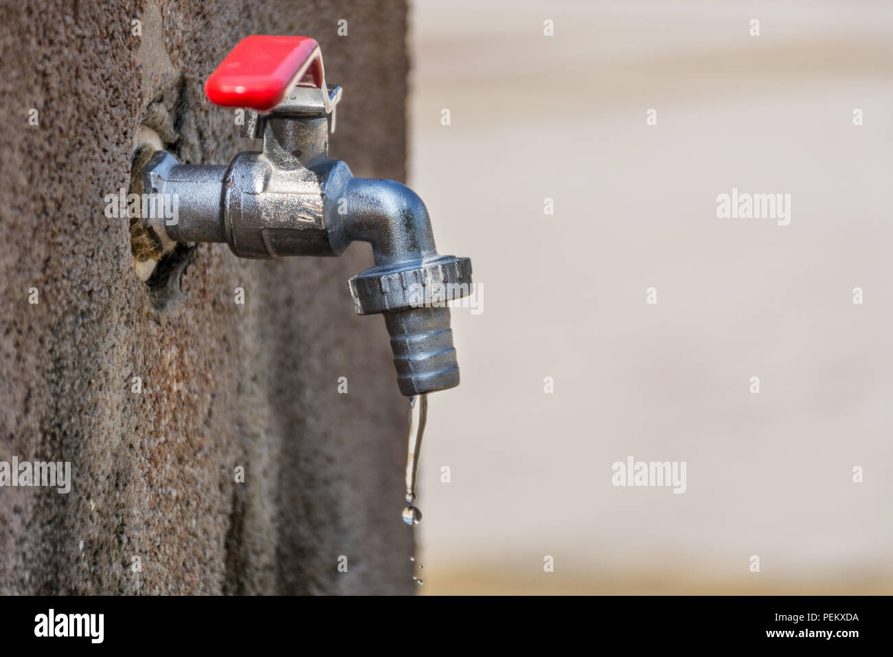 Mischbatterie mit Wassertropfen auf einem sonnigen Sommertag. Alte Tippen mit rotem Griff. Wasser sparen Konzept. Close Up, selektiver Fokus Stockfoto