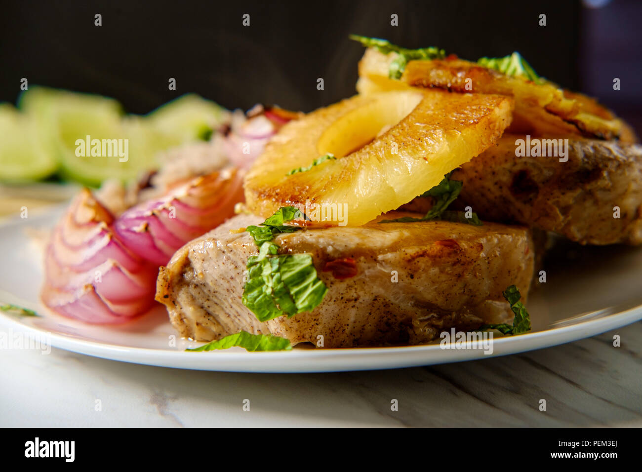 Marinierte kubanische Ananas Schweinekoteletts mit traditionellen schwarzen Bohnen Reis gegrillte rote Zwiebel und frittierte Kochbananen Chips Stockfoto
