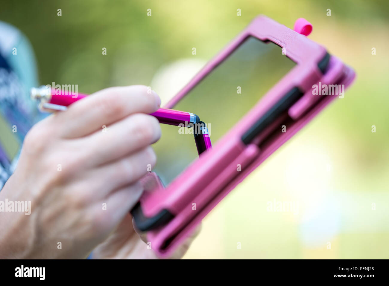 Nahaufnahme der Hand einer Frau stehen im Freien Schreiben auf dem Touchscreen eines rosa Tablette mit einem Stift. Stockfoto