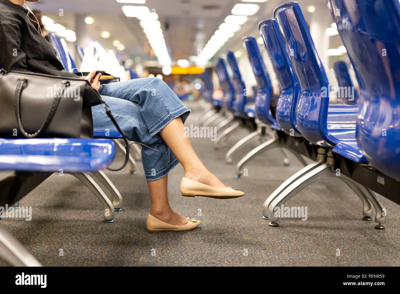 Frau sitzt im Schneidersitz mit cremefarbenen Schuhe holding Handy im Flughafen Terminal. Stockfoto