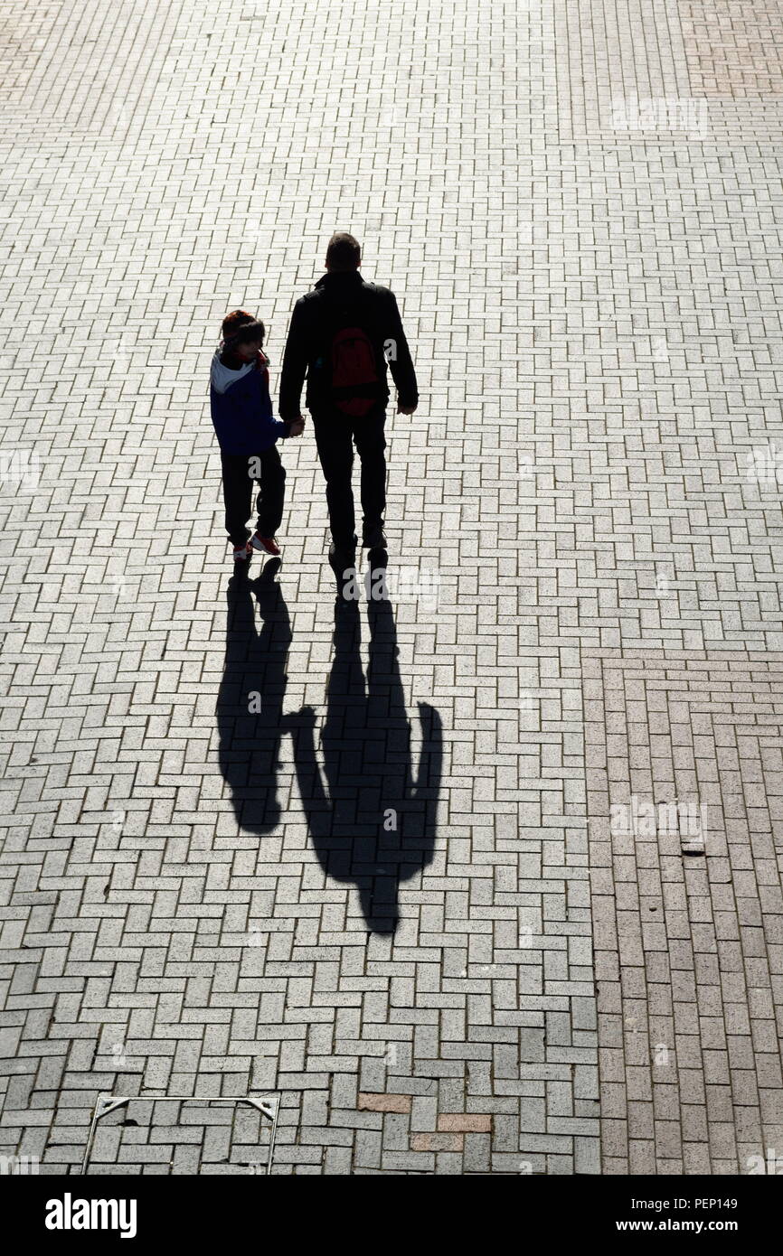 Silhouetten mit langen Schatten von Menschen gehen auf große gemauerte Pflaster Stockfoto