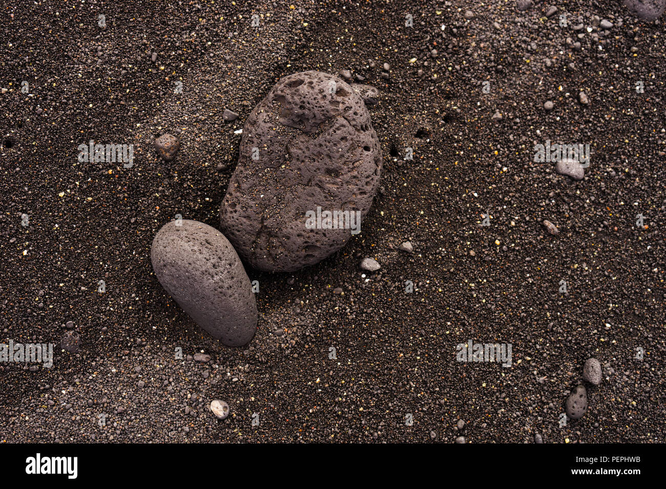 Schwarzer Sandstrand Hintergrund mit Vulkangestein Stockfoto