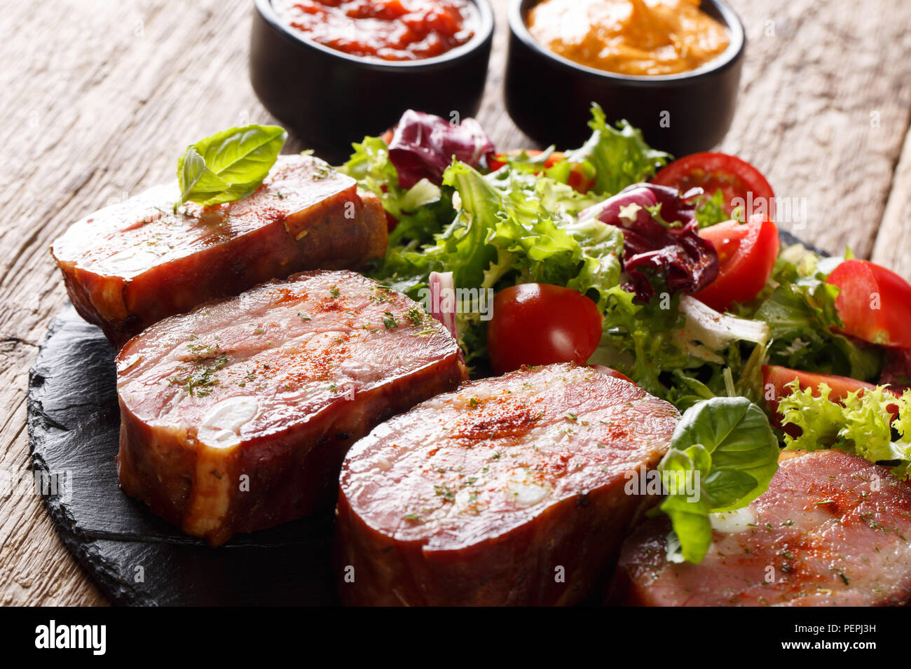 Gebratene Rippchen und frisches Gemüse Salat. Mit Ketchup und Senf auf einer Schiefertafel Teller serviert. Horizontale Stockfoto