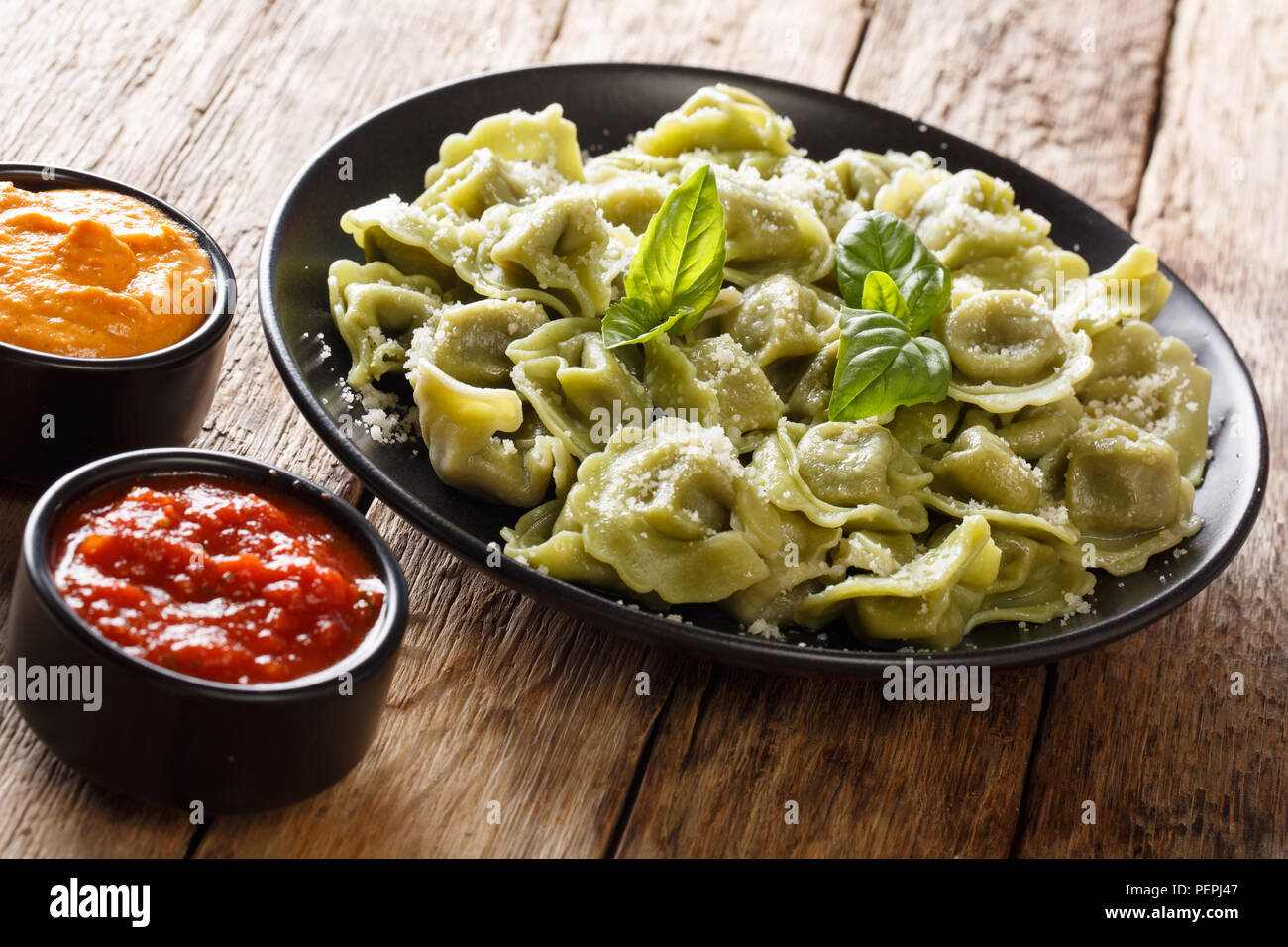 Pikanter Spinat grün Cappelletti, Ravioli, Tortellini mit Käse, Basilikum auf einem Teller, Ketchup, Senf, close-up auf dem Tisch. Horizontale Stockfoto